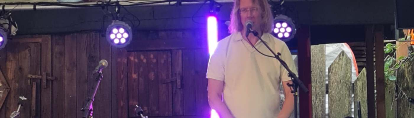 Frans van Hilten staat op een klein podium achter zijn rode Nord Stage 2 piano en zingt in een microfoon.