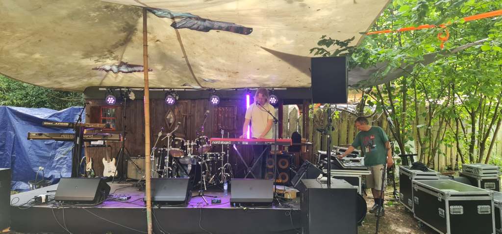 Frans van Hilten staat op een klein podium achter zijn rode Nord Stage 2 piano en zingt in een microfoon.